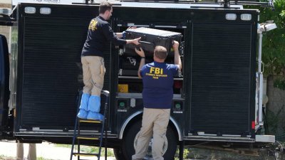美国联邦调查局（FBI）人员在准备调查被击毙嫌犯罗伯森住家时，从车上卸下装备。（图取自法新社）