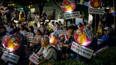 韩国首尔民众周二晚在市政厅前举行集会，高举“SOS！太平洋”的标语牌，抗议日本政府一意孤行将福岛核污水排海。（图取自法新社）