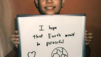 韩喆凯在照片中露出笑容，并且手握一个白板，上面写著“我希望地球会是和平的”。