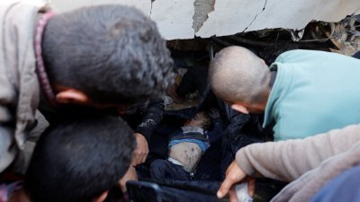 以军在周一空袭加沙南部拉法，一群巴勒斯坦人从瓦砾中拉出一名男童的尸体。（图取自路透社）