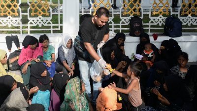 罗兴亚穆斯林难民抵达印尼班达亚齐，遭到当地居民拒绝庇护后，周一在政府办公室外的人行道上休息时领取食物。（图取自路透社）