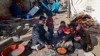 在加沙地带南部拉法，一户巴勒斯坦家庭周一在他们破损房屋外的空地上做饭。（图取自法新社）