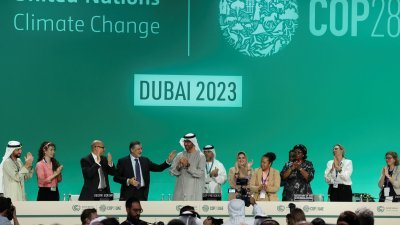 经过加时谈判，在阿联酋迪拜举行的气候峰会终于达成协议。周三的全体会议上，台上的代表鼓掌庆祝，峰会主席贾比尔（中）接受代表的祝贺。（图取自路透社）