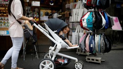一名女子推著婴儿车，在韩国首尔弘大区逛街，婴儿车内的宝宝好奇探头观察。（路透社档案照）