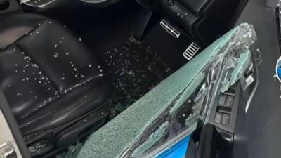 轿车驾驶座的车窗被砸，玻璃碎片掉满地。