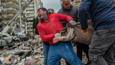 在土耳其阿达纳（Adana），一名救援人员（红衣者）周一从废墟中抬出一具遇难者遗体时难忍悲痛、大声嚎哭。（图取自法新社）