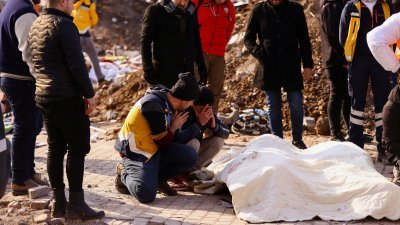 土耳其哈塔伊省卡赫拉曼马拉什的灾区里，民众悲痛地蹲在被布料盖著的遗体前。（图取自路透社）