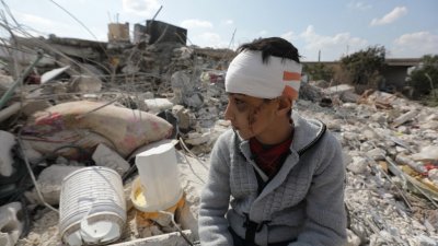 在叙利亚反抗军控制的金代里斯（Jindayris）镇，一名在强震中失去家人的受伤男童坐在已变成废墟瓦砾的家园上。（图取自法新社）