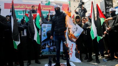 在加沙地带，一名巴勒斯坦蒙面激进分子周日踩著以色列国家安全部长的照片，同时焚烧另一张照片，谴责以色列和巴勒斯坦官员当天在约旦红海度假胜地亚喀巴举行会谈。（图取自路透社）