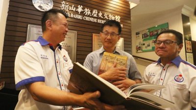 林先强（左起）向林文清展示新山中华公会出版的书籍内容，旁为李玉品。
