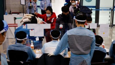 在韩国仁川国际机场，身穿防护服的工作人员检查从海外抵达的乘客。（图取自路透社档案照）