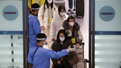 在韩国的仁川国际机场，从中国入境的旅客脖子上挂了黄色牌子，由穿著防疫服的军人指示前往检测中心。