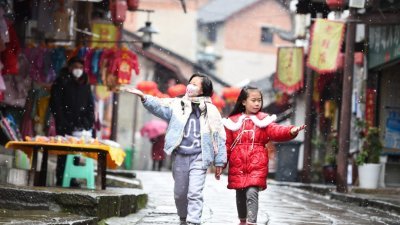 随著冷空气南下，重庆中心城区多地在周日迎来2023年首场降雪。在重庆九龙坡区的走马古镇，皑皑白雪与古镇的大红灯笼相映成趣，呈现出一派祥和喜庆的氛围。图为在重庆走马古镇，两位小朋友在雪中嬉戏。（图取自中新社）