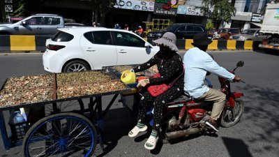 在柬埔寨首都金边，一名骑著摩哆的小贩拉著一辆装满乾河贝的手推车。（图取自法新社）