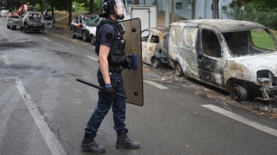 周六在巴黎郊区楠泰尔的巴勃罗·毕加索社区，一名身穿防暴装备的法国警察在被烧毁的汽车旁观看情况。（图取自法新社）