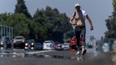 美国加利福尼亚州6月30日的气温高达摄氏38度，路上的行人难忍酷热，把上衣脱下。（图取自路透社）