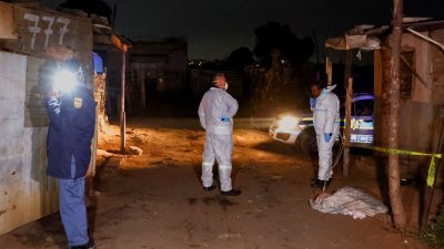 南非周三发生气体泄漏意外致死事件，身穿防护服的法医人员和警察在事发地点进行搜查，地上可看见一名被布覆盖著的儿童尸体。（图取自路透社）