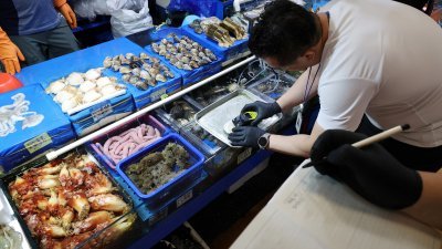 图为周四在韩国首尔鹭梁津水产批发市场，一名官员在测量从日本进口的扇贝的辐射水平。（图取自路透社）