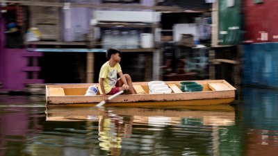 在菲律宾马尼拉大都会马拉翁，一名男孩上周二划船穿过被洪水淹没的Artex Compound取清洁水。（图取自路透社）