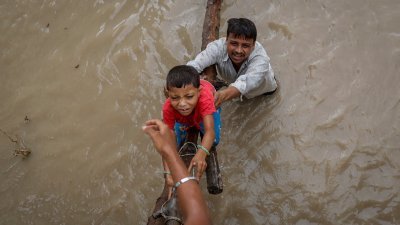 印度新德里周三遭季风暴雨袭击，导致亚穆纳河水位上涨至历史新高，一名男子帮助他儿子爬上一座正在建设中的天桥。（图取自路透社）