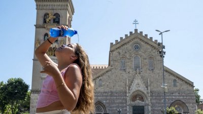在意大利西西里岛墨西拿的一座教堂前，一名女孩周日将一瓶水倒在脸上和头上降温。（图取自法新社）