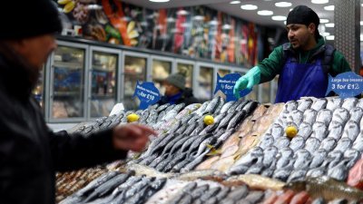 3月9日在英国伦敦东南部的Lewisham市场，一名工人在为选购鲜鱼的顾客服务。（图取自路透社档案照）