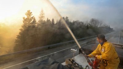 在加拿大新斯科舍省谢尔本县，当地消防员上周五沿著103号高速公路向正在燃烧的野火喷水。（图取自新斯科舍/路透社）