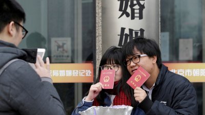 2017年2月14日情人节当天，中国北京一对持有结婚证的新人在婚姻登记处外合影留念。（图取自路透社档案照）