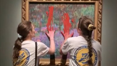 环保组织“恢复湿地”发布视频，两名活动人士在瑞典斯德哥尔摩的国家博物馆，用手将红色颜料抹在莫奈名画《吉维尼的艺术家花园》的防护玻璃上。（“恢复湿地”面子书视频截图）