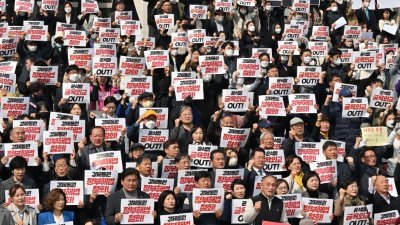 在首尔的国民议会举行的反政府集会上，韩国立法者和抗议者周二举著标语牌，谴责尹锡悦政府针对日本二战时期强征劳工受害者赔偿问题的解决方案。（图取自法新社）