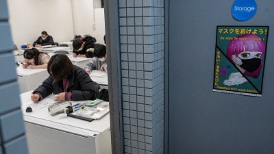 2月6日，在东京原宿地区的东京设计学院，学生们参加漫画艺术设计课程。课室门外贴了一张提醒人们戴口罩的海报。（图取自法新社）