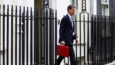 英国财长亨特当地时间周三走在唐宁街时，手上拎著装有春季预算案的红色箱子。（图取自路透社）