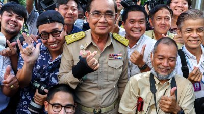 在泰王批准解散国会的法令后，泰国首相巴育周一在曼谷与媒体成员合影时用手比心。巴育右手最近感染炎症入院，被治疗后无大碍，但仍包扎手套。（图取自路透社）