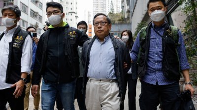 香港前支联会副主席何俊仁（前排右2）周二上午被补。他被反手锁上手铐，由警方国安处人员带走。（图取自路透社）
