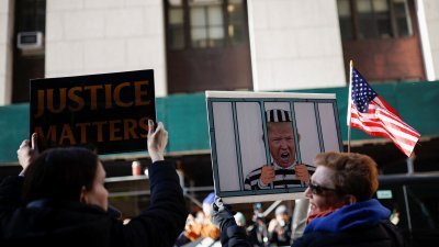 示威者周二拿著特朗普坐牢的示意图，聚集在纽约地方检察官办公室外示威。（图取自路透社）