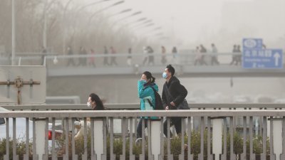 北京在周三遭遇大风和沙尘天气，市民戴著口罩出行。（图取自中新社）