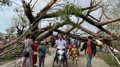 在缅甸若开邦皎道镇，热带气旋“摩卡”周一登陆后造成广泛的破坏，当地居民从被强风吹至折断的树木旁走过。（图取自法新社）