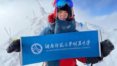16岁的徐卓媛拿著学校的横幅登山。（图取自网络）