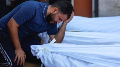 加沙地带南部汗尤尼斯的一家医院内，一名巴勒斯坦男子难过地跪在多具被白布包裹的遗体旁。（图取自路透社）