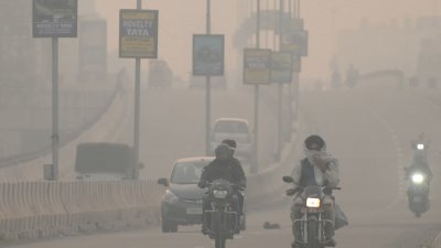 周一在印度西北部旁遮普的阿姆利则，人民在烟雾弥漫的道路上出行通勤。（图取自法新社）