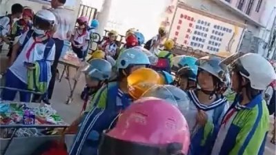 网传视频显示，在小学校门口，几十名学生走路时纷纷戴著头盔。（图取自央广网）