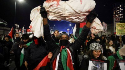 一名示威者当地时间周六在英国伦敦，参加声援巴勒斯坦人的集会时高举自制裹尸布。（图取自路透社）