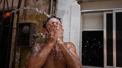 图为上周五在巴西里约热内卢，罗西尼亚贫民窟的一名居民于酷热天气期间在街上用水管降温。当局报告，里约热内卢的高温达到创纪录的摄氏58.5度。（图取自法新社）