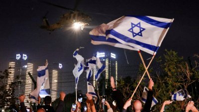 以色列民众当地时间周五，朝著载有获释人质的直升机，兴奋地挥舞以色列国旗。（图取自路透社）