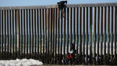 一名移民当地时间周一在墨西哥蒂华纳，试图翻越边境墙进入美国申请庇护。（图取自路透社）
