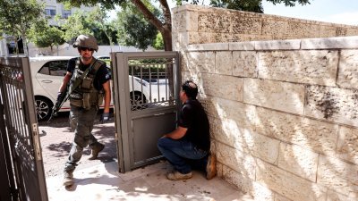 在以色列耶路撒冷西部城镇梅瓦塞雷特锡安，当警报声响起，一名男子躲在墙边，一名以色列军人迅速走进铁门内。（图取自路透社）