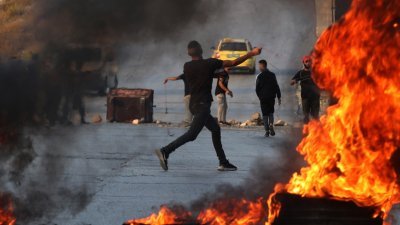 一名巴勒斯坦少年周日在被以色列占领的约旦河西岸，朝以色列士兵投掷石块。（图取自法新社）