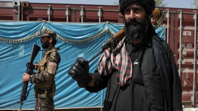 图为去年在喀布尔的一个配送中心，塔利班武装分子正在站岗，人们等待接收从中国捐赠的麻袋大米，作为人道援助物资。（路透社档案照）