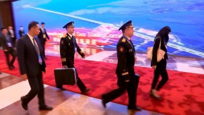 两名俄罗斯海军军官周三在陪同总统普京出席北京“一带一路”国际合作高峰论坛时，提著被认为是核按钮手提箱。（图取自RUPTLY FOR RUSSIAN POOL/路透社）