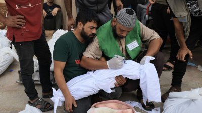 在加沙地带中部的阿克萨烈士医院太平间前，一名男子在以色列袭击中丧生的一名儿童的裹尸布上写下名字。（图取自法新社）